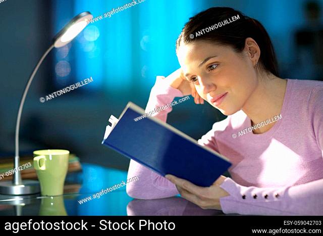 Concentrated woman reading a paper book at home in the night