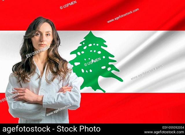 Medicine in Lebanon. Happy beautiful female doctor in medical coat standing with crossed arms against the background of the flag of Lebanon