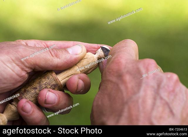 Man carving a small wooden figure, close-up with hands, wood and carving knife. Värmland, Sweden, Europe