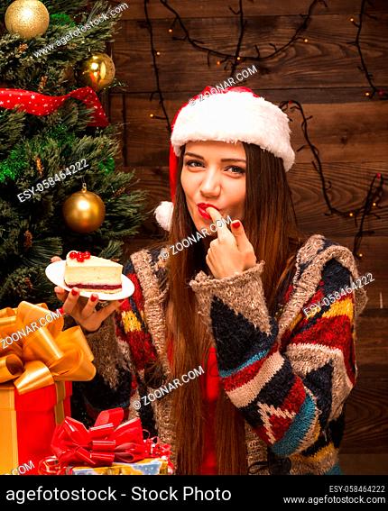 New Year and Christmas concepts. Beautiful girl eating delicious cake while sitting near New Year tree and Christmas presents and gifts