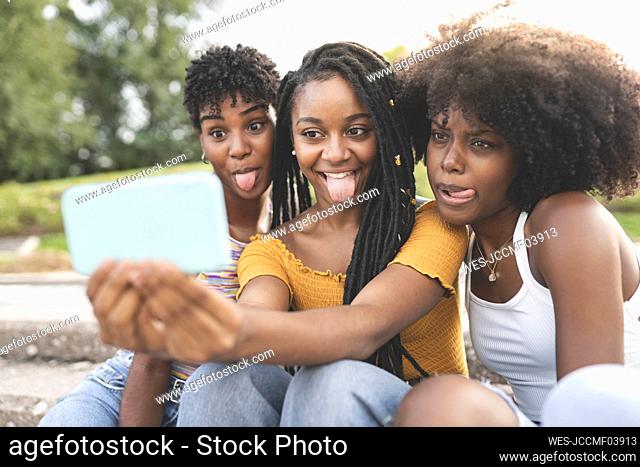 Young women sticking out tongue while taking selfie through mobile phone at park