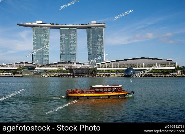 Singapore, Republic of Singapore, Asia - A traditional excursion boat (Bumboat) sails by the iconic Marina Bay Sands Hotel as it cruises on the Singapore River...