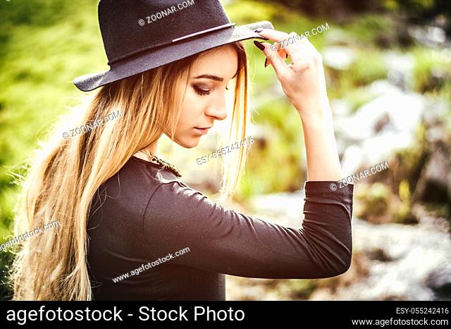 Pretty blonde young woman outdoor in city park, wearing short black dress and fedora hat