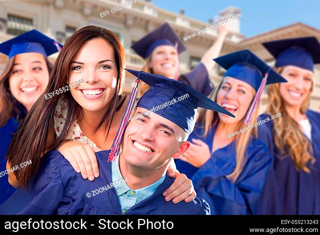 Proud Male Graduate In Cap and Gown with Girl Among Other Graduates Behind