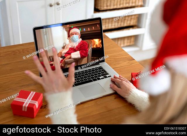 Woman in Santa hat having a video chat with Santa Claus wearing face mask on her laptop at home
