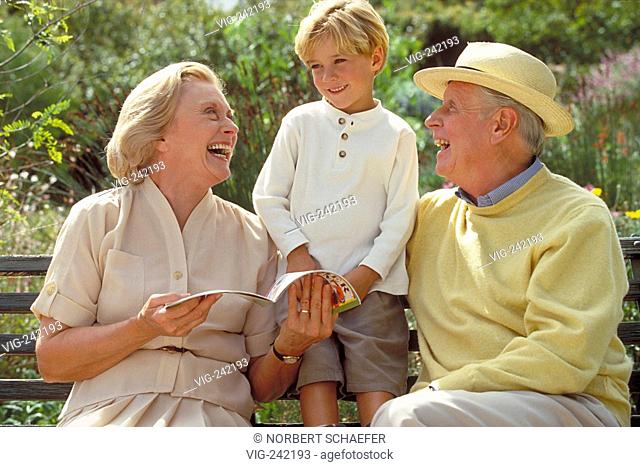 outdoor, park-scene, 6-year-old blond boy stands between his grandparents sitting on a park bench reading a brochure  - GERMANY, 19/09/2004
