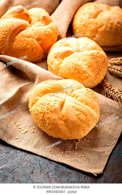 Delicious fresh buns with sesame seeds and ears of wheat on a linen napkin