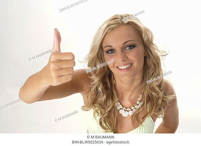 blonde young woman looking into the camera, holding up her thumb