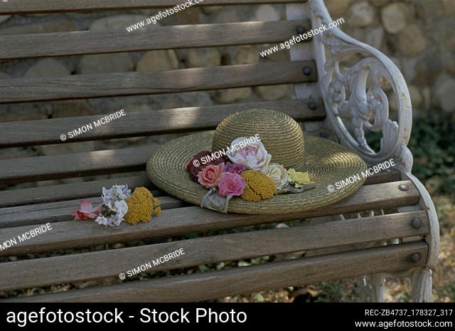 A detail of a wrought iron bench seat with wooden slat seating, straw hat decorated with flowers