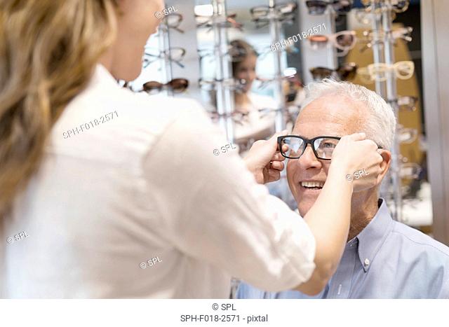 Optician putting glasses on senior man