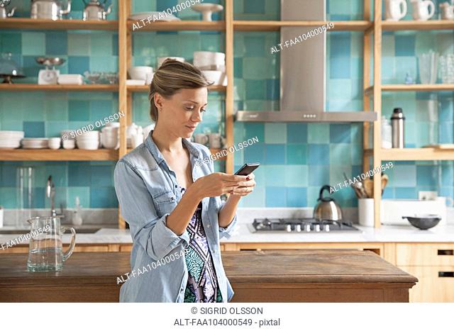 Young woman standing in kitchen with cell phone