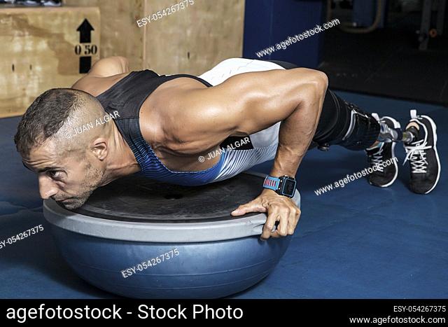 Confident adult sportsman with artificial leg limb doing push-ups on bosu ball