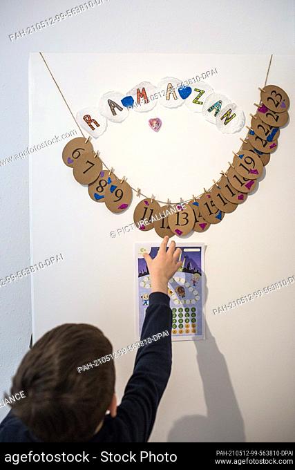 PRODUCTION - 10 May 2021, North Rhine-Westphalia, Minden: The child looks at a Ramadan calendar, on the back of which his parents have written tasks for the...