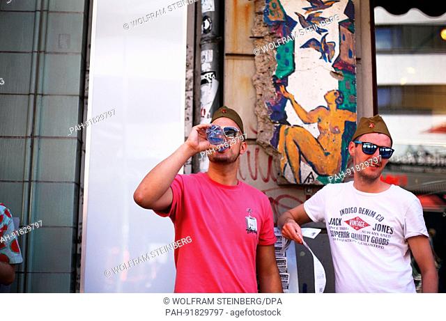 British tourists wear sunglasses and Russian military caps, they bought here from a souvenirs dealer, in front of the Berlin Wall Museum at Checkpoint Charlie...