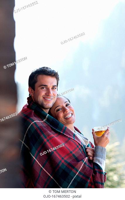 Portrait of smiling couple wrapped in a blanket and drinking hot cider on porch