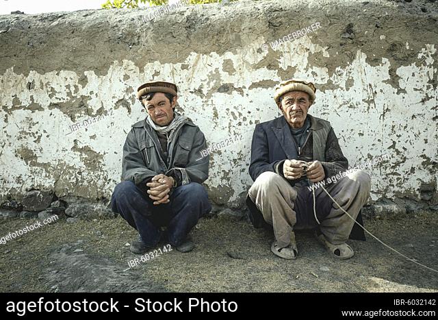 Two men squatting in front of a clay wall, sedentary Wakhi, Wakhan Corridor, Saradh-e-Broghil, Afghanistan, Asia