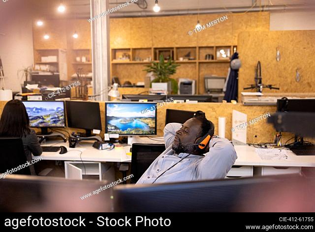 Businessman in headset reclining with hands behind head in office