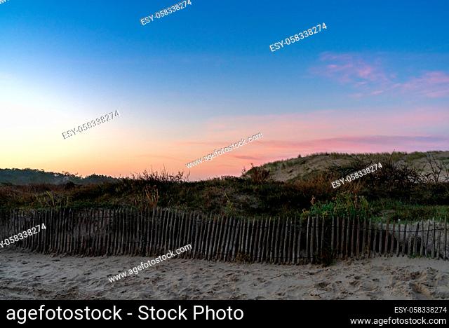 A wooden palisade fence and beach and sand dunes at sunrise