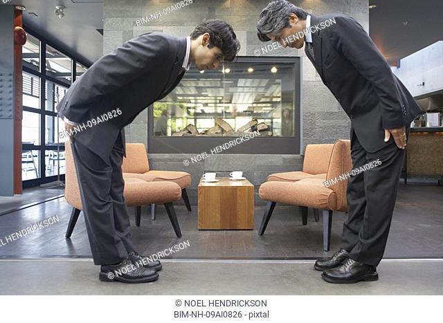 Two businessmen bowing to each other in cafe