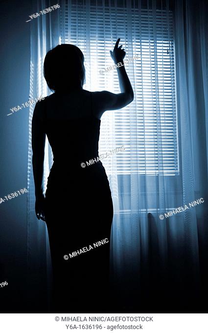 Silhouetted woman standing by window reaching for light