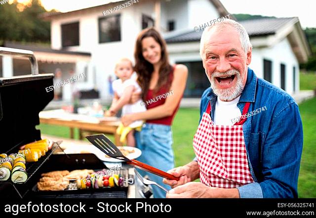 A portrait of multigeneration family outdoors on garden barbecue, grilling