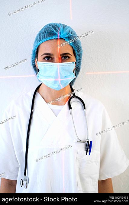Young female doctor with laser light on face against wall at clinic