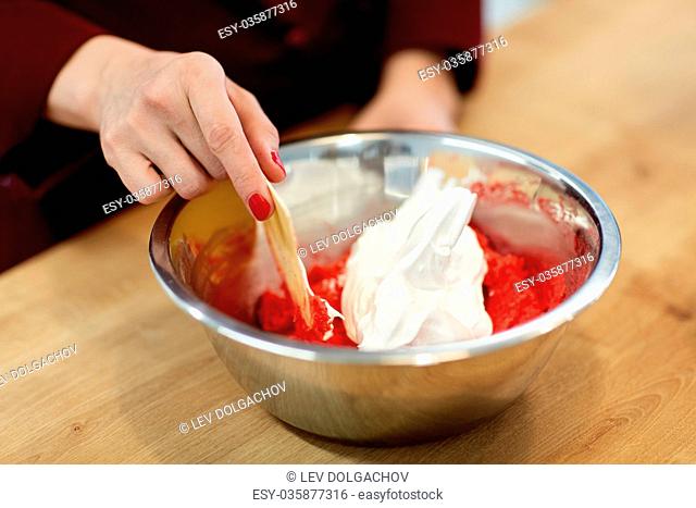 cooking, food and people concept - chef with spatula stirring macaron batter or cream in bowl at pastry shop