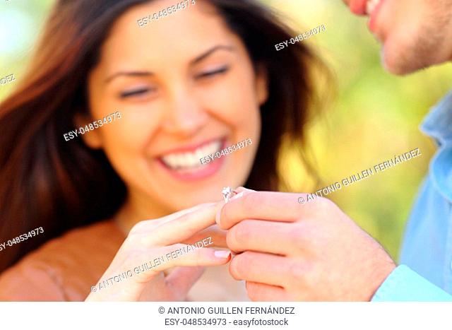 Happy man putting engagement ring to his glad girlfriend after proposal outdoors in a park