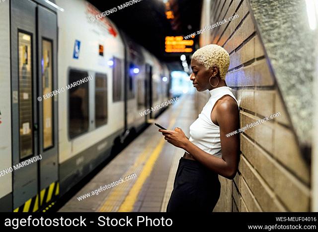 Woman using mobile phone while leaning on wall at subway station