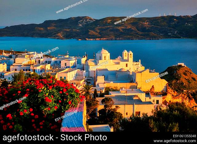 View of Plaka village on Milos island over red geranium flowers on sunset. Plaka town, Milos island, Greece