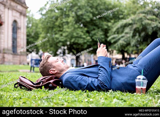 Young businessman using mobile phone while lying on grass
