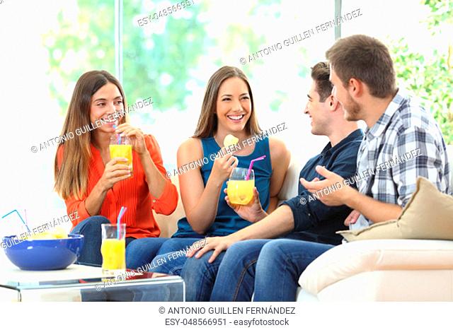 Group of happy friends talking eating chips and drinking refreshments sitting on a couch in the living room at home