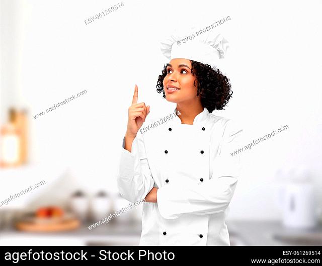 smiling female chef pointing finger up in kitchen