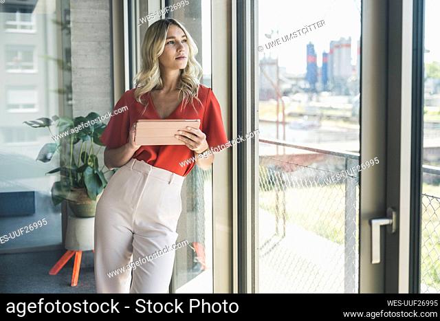 Young businesswoman with tablet PC leaning on window in office