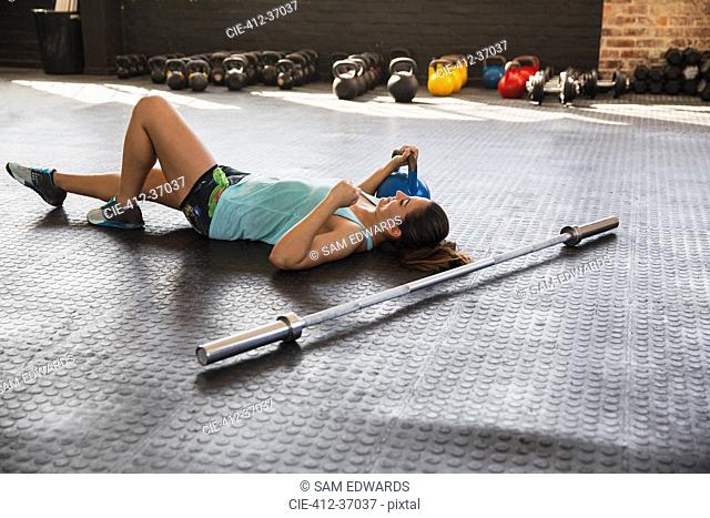 Young woman resting, laying on gym floor next to barbell and kettle bell