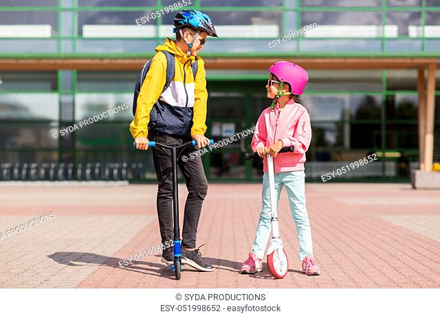 happy school children in helmets riding scooters