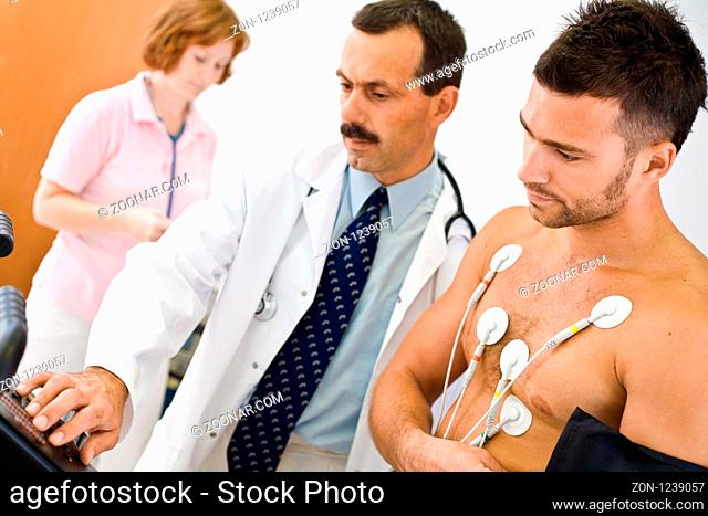Medical team performing an EKG test on young male patient. Real people, real locacion, not a staged photo with models. Focus is placed on the patient