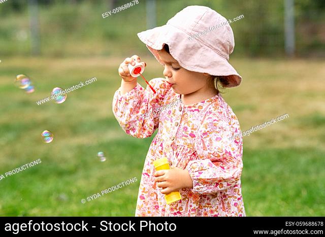 happy baby girl blowing soap bubbles in summer