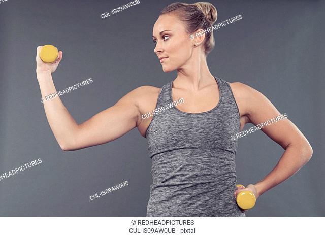 Young woman working out with dumbbells, grey background
