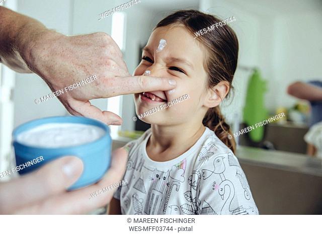 Father putting facial cream on daughterâ€™s face