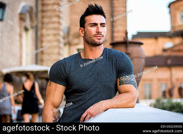 Attractaive muscular man with tattoo posing in European city center, Turin, Italy, looking at camera