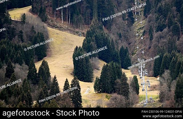 05 January 2023, Bavaria, Garmisch-Partenkirchen: The ski slope next to the gondola is green. In many winter sports areas it is currently rather green than...