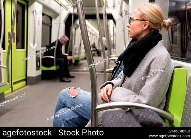 Beautiful blonde caucasian lady wearing winter coat and scarf traveling by metro. Public transport
