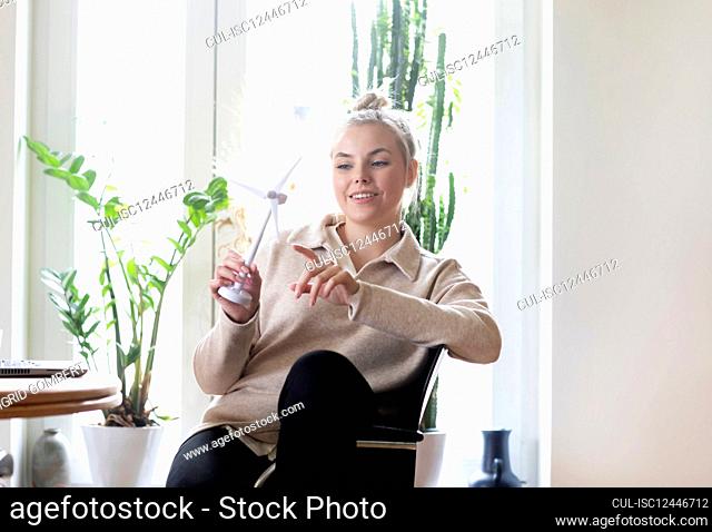 Smiling woman holding wind turbine model at home
