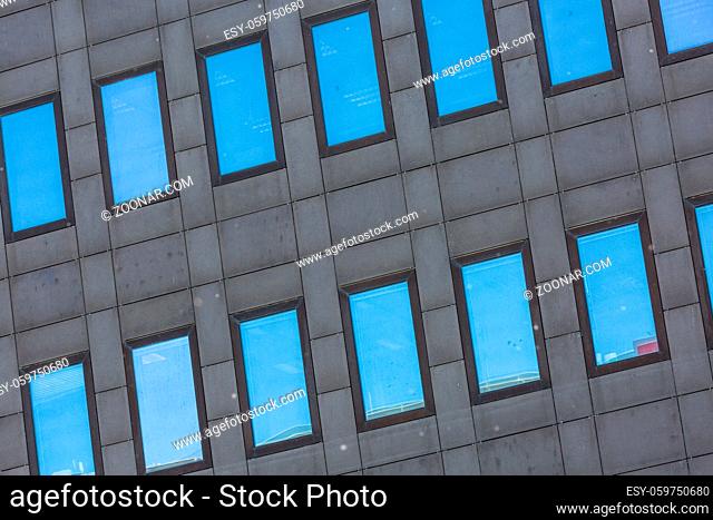 Windows of a tall grey building reflecting the blue sky
