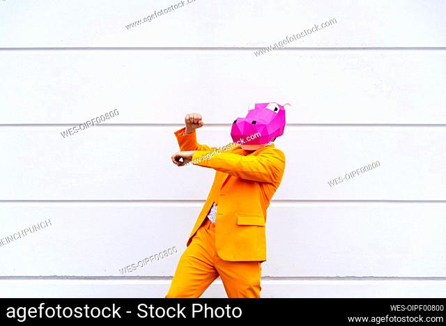 Man wearing vibrant orange suit and hippo mask dancing in front of white wall