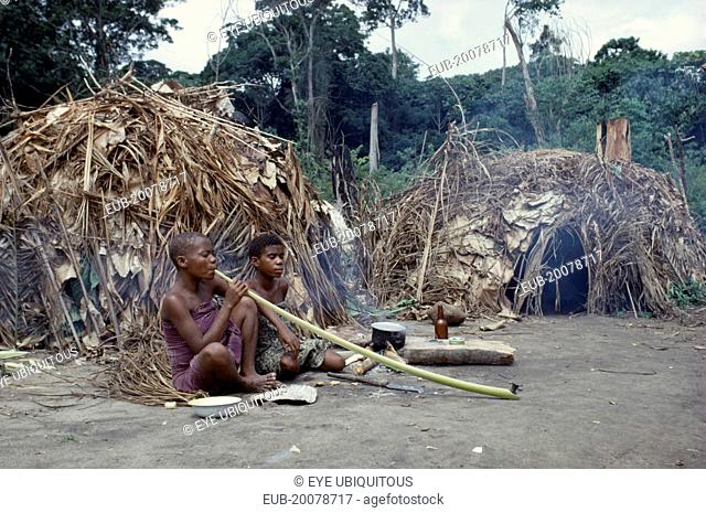Pygmy women smoking tobacco outside thatched, domed huts
