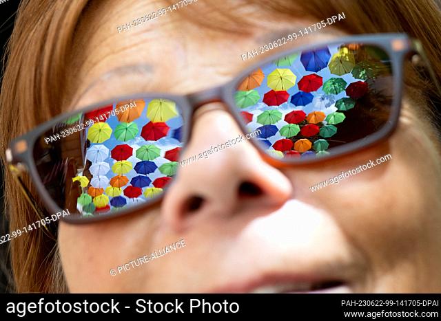 PRODUCTION - 20 June 2023, Rhineland-Palatinate, Mainz: Umbrellas from the ""Umbrella Sky"" campaign are reflected in a woman's sunglasses in Alststadt