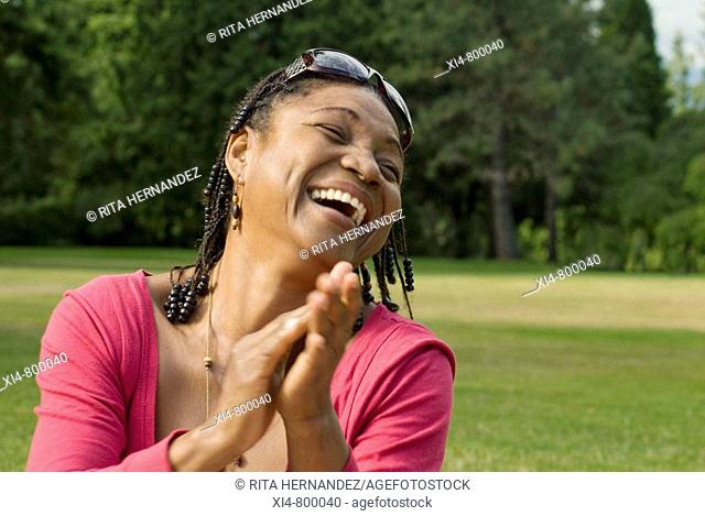 Mature African Hispanic woman clapping She is seated in the green grass and laughting