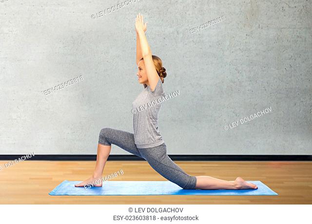 fitness, sport, people and healthy lifestyle concept - happy woman making yoga in low lunge pose on mat over room or gym background